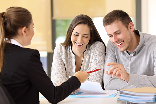 Photo of young couple signing loan documents with female loan officer