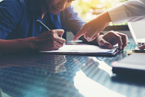 Photo of young man signing documents with hand pointing to signature line