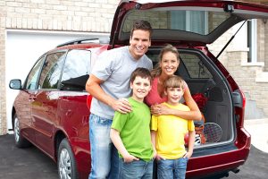 Mom Dad and two boys smiling in front of new minivan